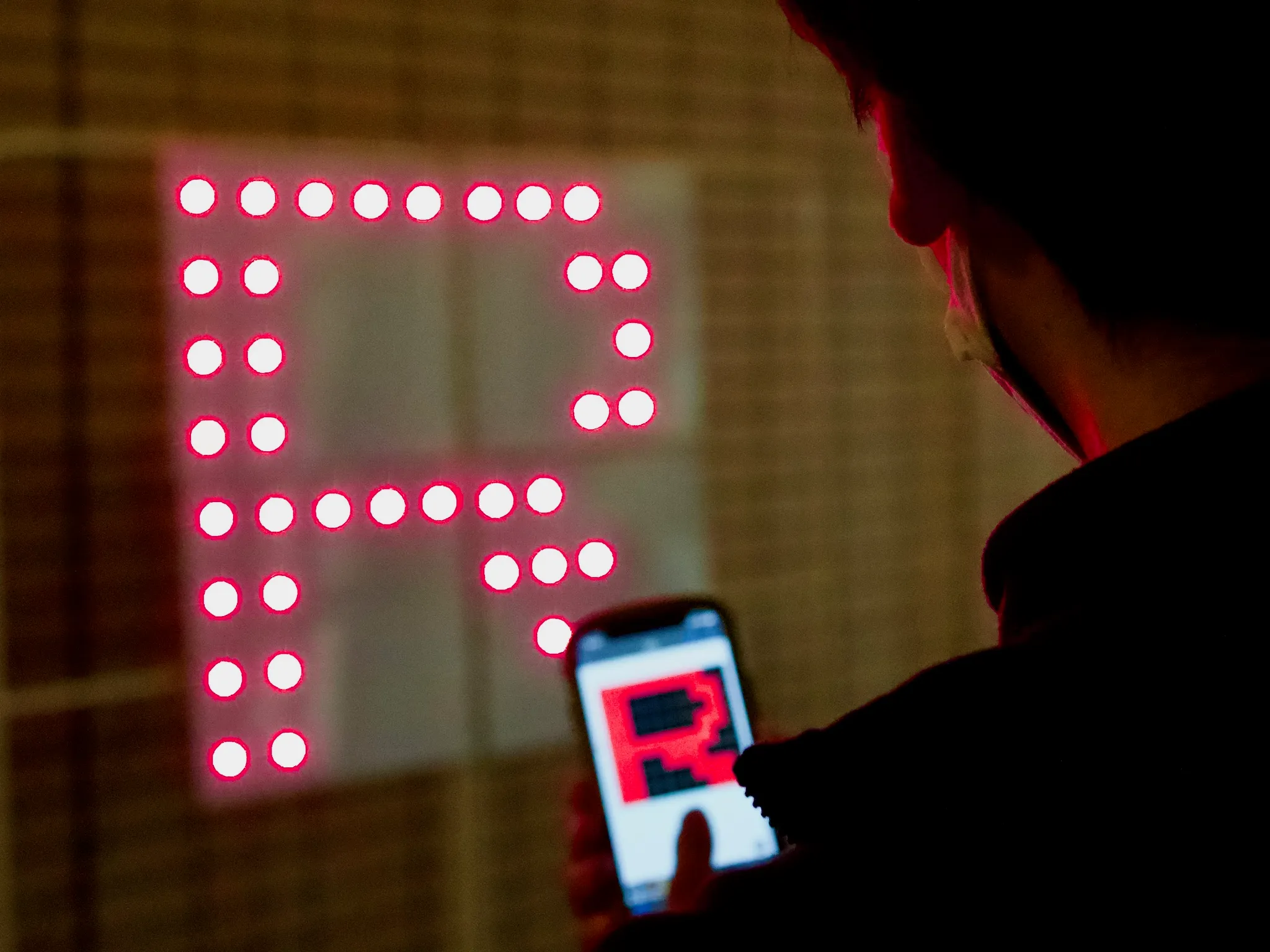 赤く点灯する格子状のLEDボードをスマートフォンで操作する様子
